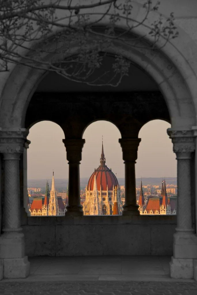 Black-and-white stone arches framing a red-domed building glowing in warm evening light.