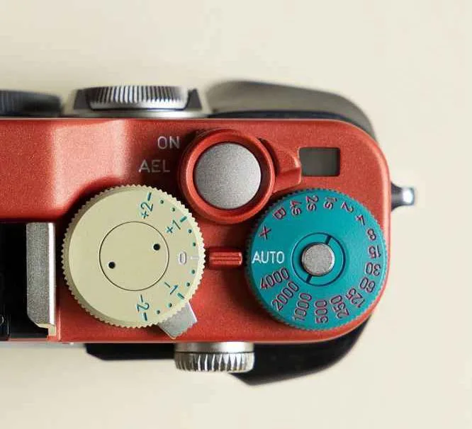 Top view of a red camera body with cream and teal dials, on a pale background.